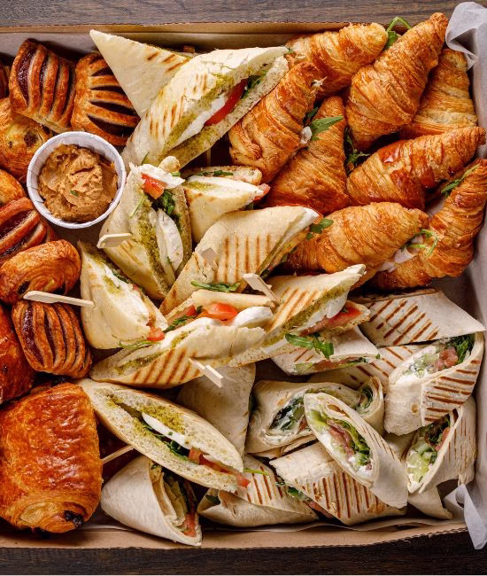 Assorted croissants, pastries, and wrap sandwiches arranged in a catering tray