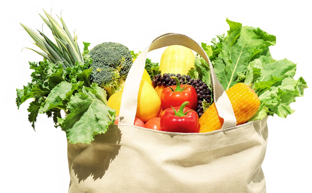 Reusable canvas grocery bag filled with fresh fruits and vegetables including leafy greens, tomatoes, broccoli, corn, and berries