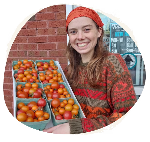 Young woman smiling and holding cartons of cherry tomatoes outside a storefront