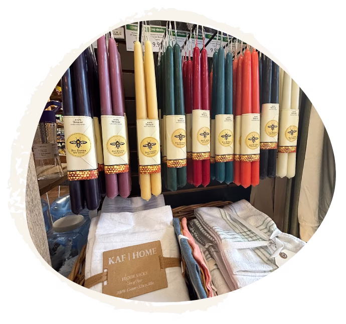 Colorful taper candles displayed on a store shelf above folded kitchen towels and home linens